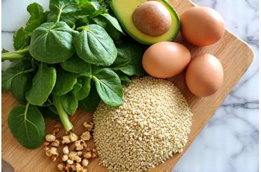 Svetle, prirodne namirnice bogate B vitaminima: spanać, avokado, jaja, losos, prikazani na drvenoj dasci.